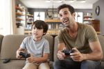 Father And Son Sitting On Sofa In Lounge Playing Video Game