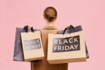 Rear view of unrecognizable woman with hair bun carrying black Friday paperbags on shoulders while leaving store