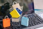 Five paper shopping bags and a shopping cart on a laptop keyboard.